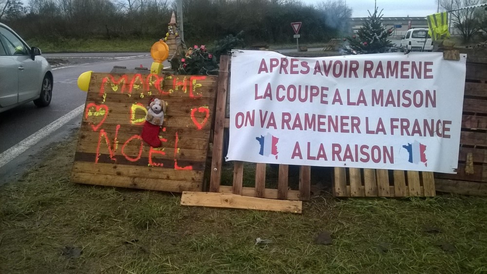 CARNETS INSITUÉS: Suspended Spaces 0.5 | Ce carnet s'inscrit dans une série de micro-récits récoltés et soulevés en images sur des sites vacants réinvestis et occupés de manière autonome ou informelle.
Ce travail est initié par Cynthia Montier.
Ce carnet reprend sous la forme de micro-publications l'idée de cartes postales, de mémoire vagabonde et clandestine en circulation directe, instantanée dans un premier temps via la plateforme Archipel, puis transitée sur Instagram; Elle sera imprimée et éditée dans un deuxième temps sous la forme de petites éditions nomades et volatiles à faire voyager, cette fois-ci à partir d’objets photographiés en fragments et sélectionnés par les habitants de la zone occupée.
Intervention sur le site du rond point à la sortie de l'A4, dans la commune d’Ennery (57).
&quot;Situation relevée lors d’une promenade opportune dans la commune d’Ennery. Un matin de réveillon, j'aperçois au loin un feu de foyer s'échapper de barricades édifiées, là où se déploie comme une parade lumineuse et typographique, mêlant en jeux ponctués feux de signalisations et façades de camions embouteillés. Je décide de me rendre sur le site. J’atterris alors sur le rond point principal d'un carrefour situé à la sortie de l'autoroute A4, investi par des manifestants du mouvement gilet jaunes. La rencontre occasionne de furtifs échanges informels, suivie d'une visite courtoise de la zone échafaudée.
Les manifestants en fête avaient alors aménagé une sorte de zone récréative pour l'occasion, entre aire de repos et aire de transit, associant alors la résistance au plaisir.
Les itinérants routiers de passages se voient alors contraints de s'arrêter au carrefour barré pour partager chocolat chaud et sablés de Noël confectionnés par les occupants, ou faire un tour au marché de Noël &quot;Gilets Jaunes&quot;.
La créativité avec laquelle est initiée cette enthousiaste fortification s'établit d'avantage comme un portail que comme un mur, initiant des temps de rencontres autonomes et fortuits à l'épicentre de nos échangeurs.
À partir de combinaisons et d'assemblages inventifs, grâce à la force de l'imaginaire et à une économie du don, les habitants et riverains locaux se branchent aux groupe pour alimenter leur terre-plein de leurs encombrants en guise de terreau fertile.
Ce périmètre suspendu véhicule l'ambition d'un chantier inédit en constante transition et reconstruction, échappant ainsi à la fixité et à l'immuabilité des positionnements économiques qu'ils s'attachent à débâtir. Cet habitat entropique est promis aux lois de la circulation et du libre-échange, en installant ses fondations temporaires à la lisière de périphéries vivantes et en intersection d'agglomérations interférées. L'emplacement hétérogène composant ainsi librement avec l'obsolescence de ses circonférences, installations temporaires et signalétiques passagères, événements et occasions routières&quot;